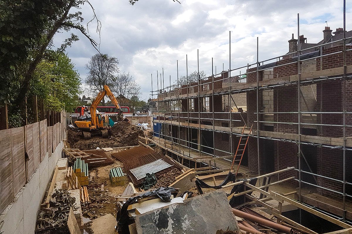 Hodford Road yellow excavator adjacent to brick building under construction with steel mesh and scaffolding