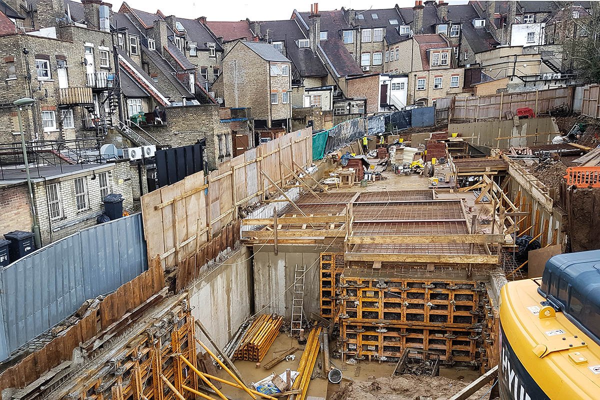 Hodford Road steel and concrete basement construction site surrounded by timber and steel hoarding and existing brick buildings