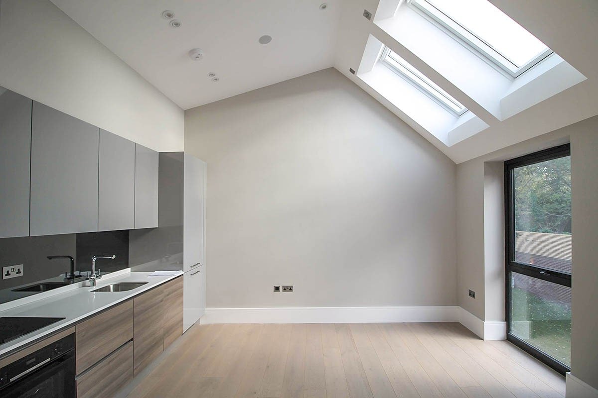 Hodford Road vaulted ceiling grey walled room with white ceiling and 2 skylights, kitchen facing black frame windows